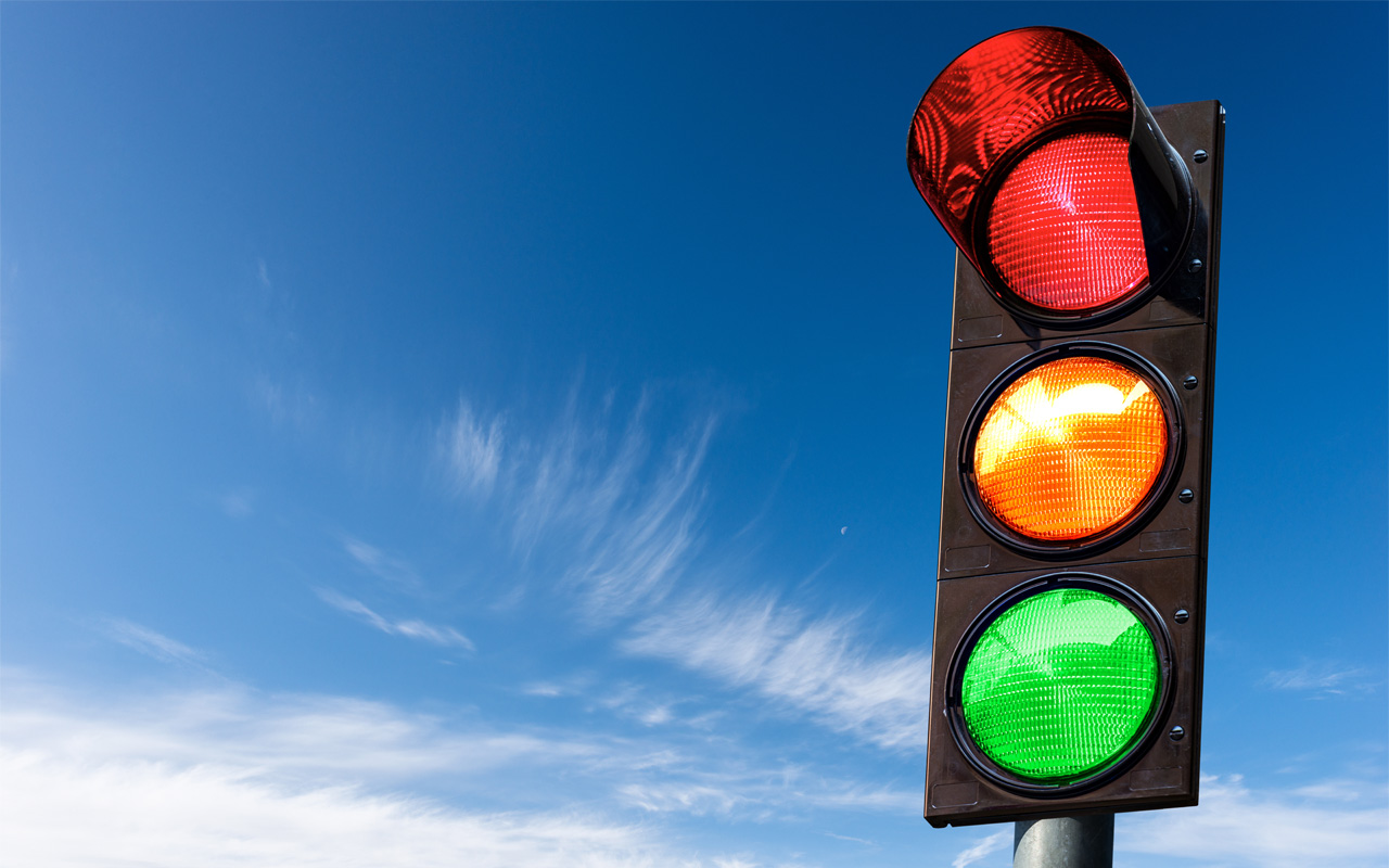 Stop light with red, yellow, and green lights shining against a blue sky.