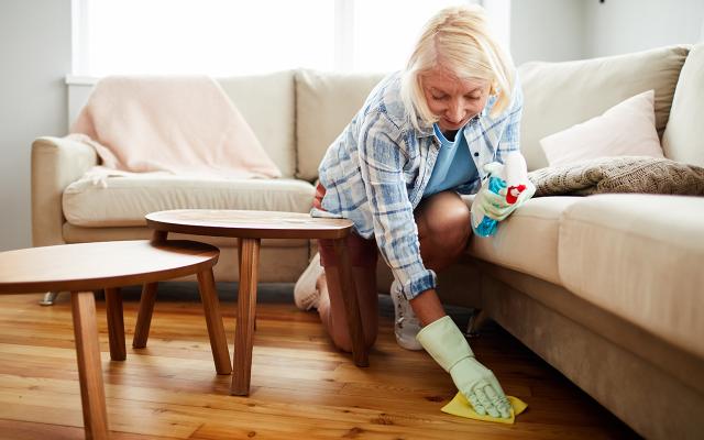 Individual cleaning a wooden floor with a cloth and spray bottle in a living room 